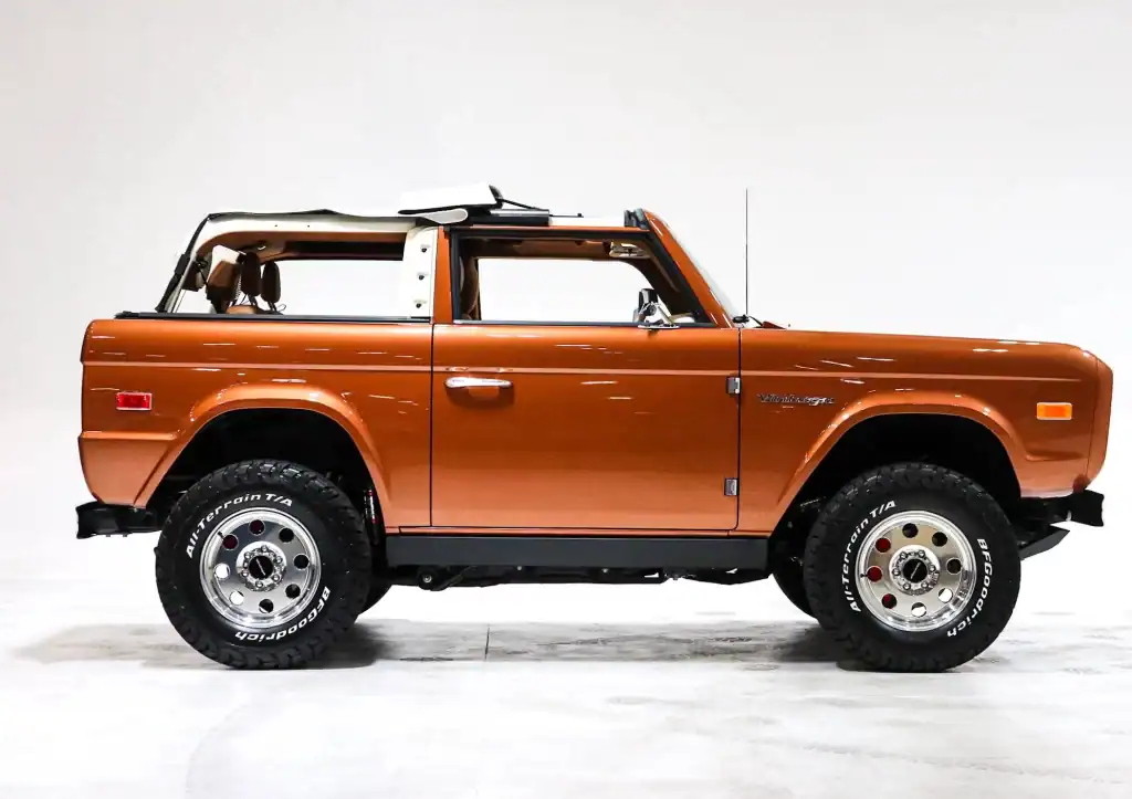Rust-colored vintage Jeep Wagoneer with classic design and rugged tires on a plain white background.