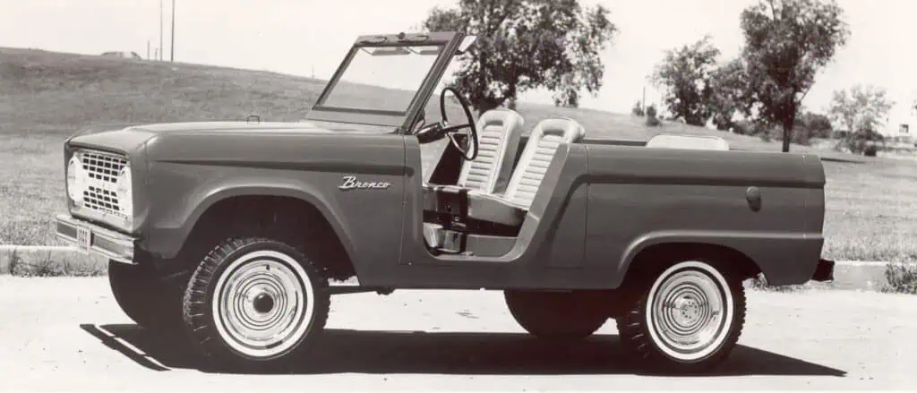 Vintage vintage Ford Bronco classic car with open side view, black and white photograph, retro style, outdoor setting in the countryside, historical automobile design.