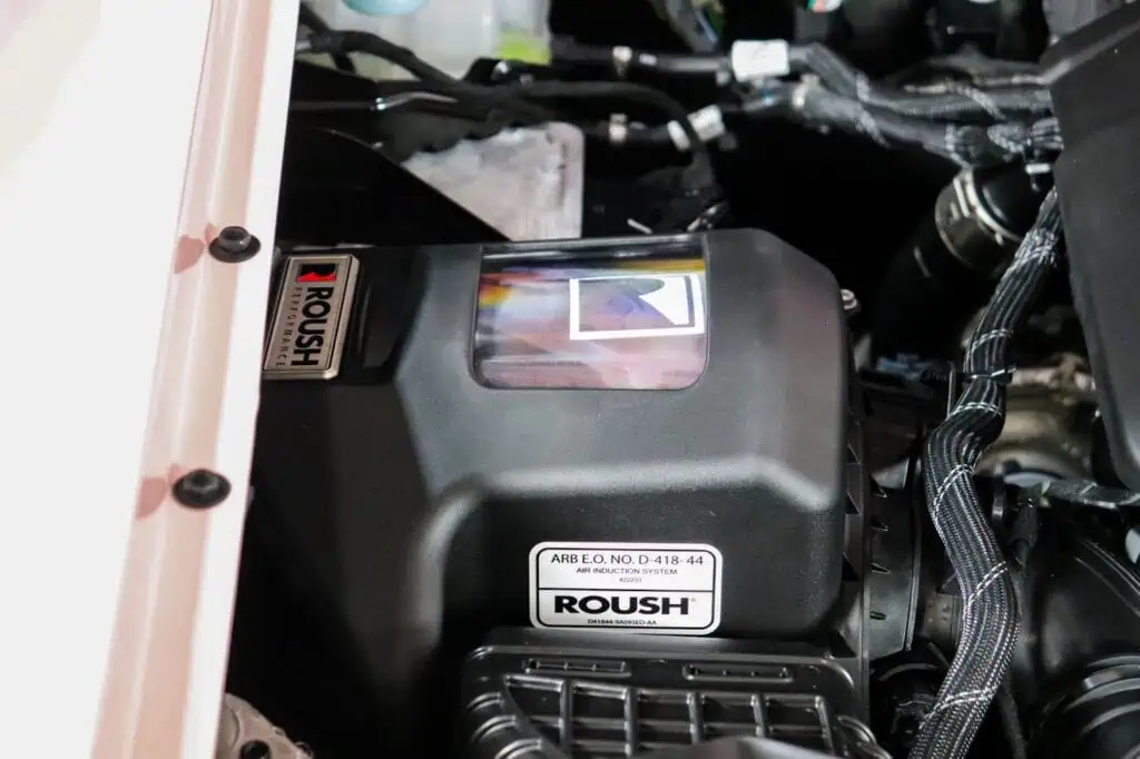 Roush air induction system engine bay with black components and branding for vintage modern automotive style.