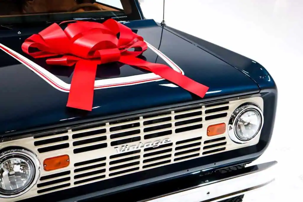 Vintage car with a large red ribbon bow on the hood, classic design, front grille, headlight, and retro style. Perfect for vintage modern automotive decor.