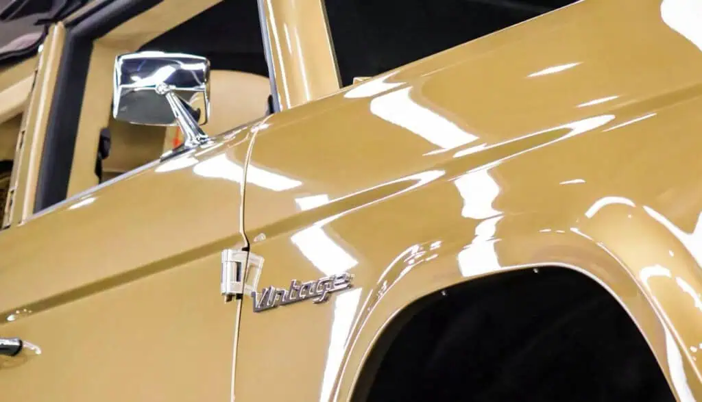 Vintage Modern classic car in gold color with chrome accents and vintage badge, showcasing mid-century automobile design at a collectible car show.