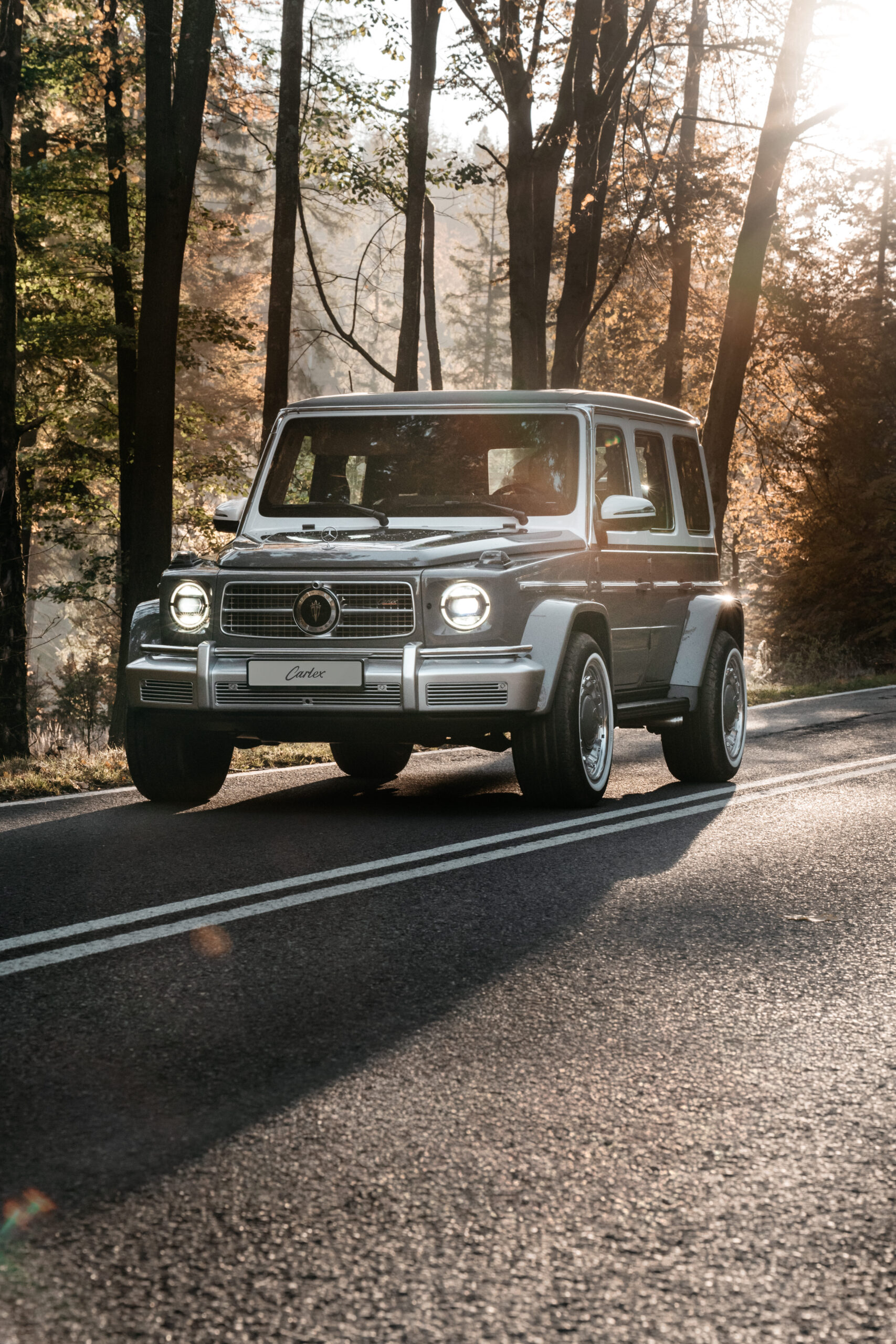 Luxury vintage Mercedes-Benz G-Class SUV parked on a forest road with sunlight filtering through trees.