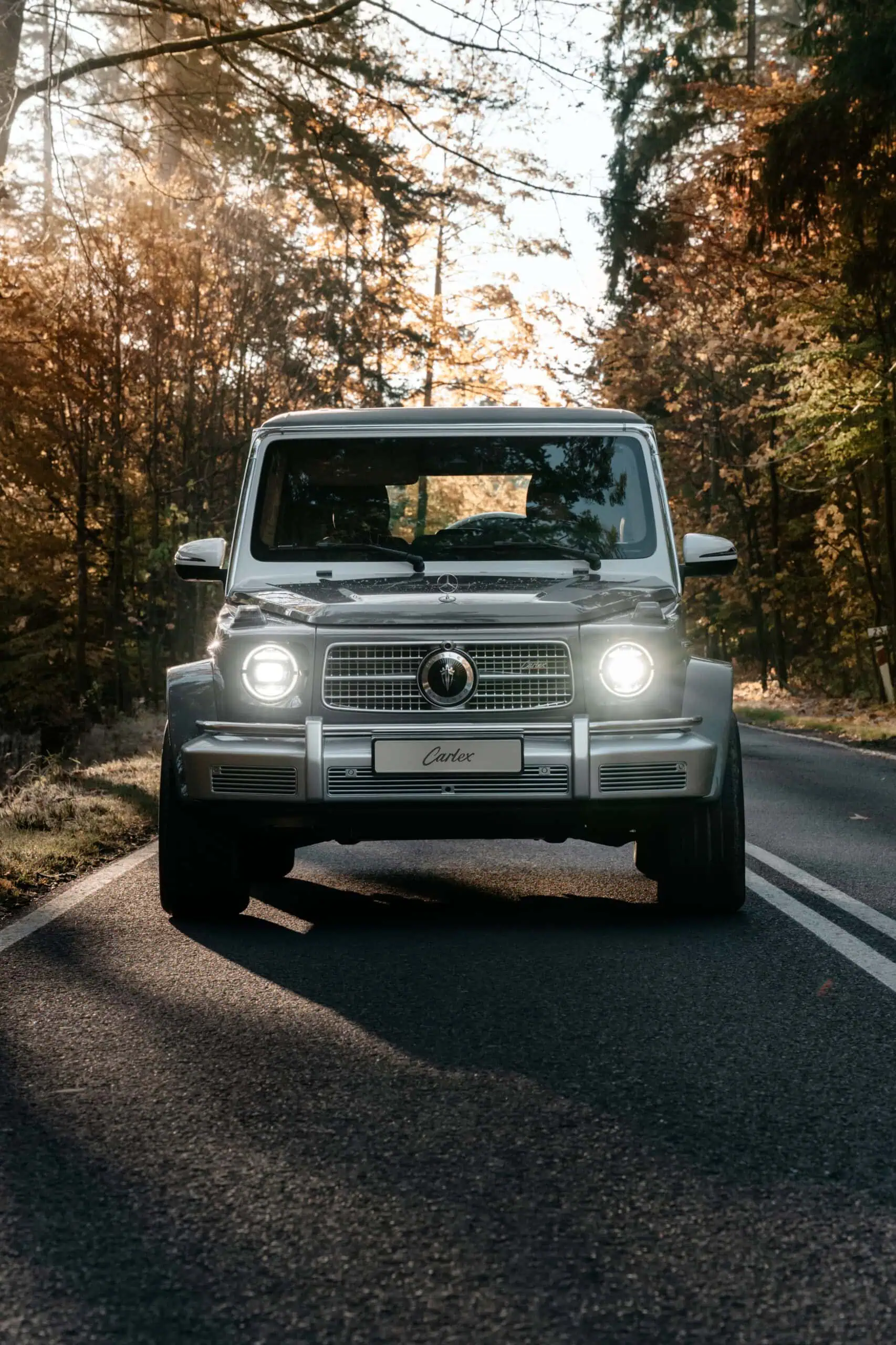 A modern vintage-style luxury car driving through a scenic forest road surrounded by autumn foliage, emphasizing timeless design and eco-friendly journeys.