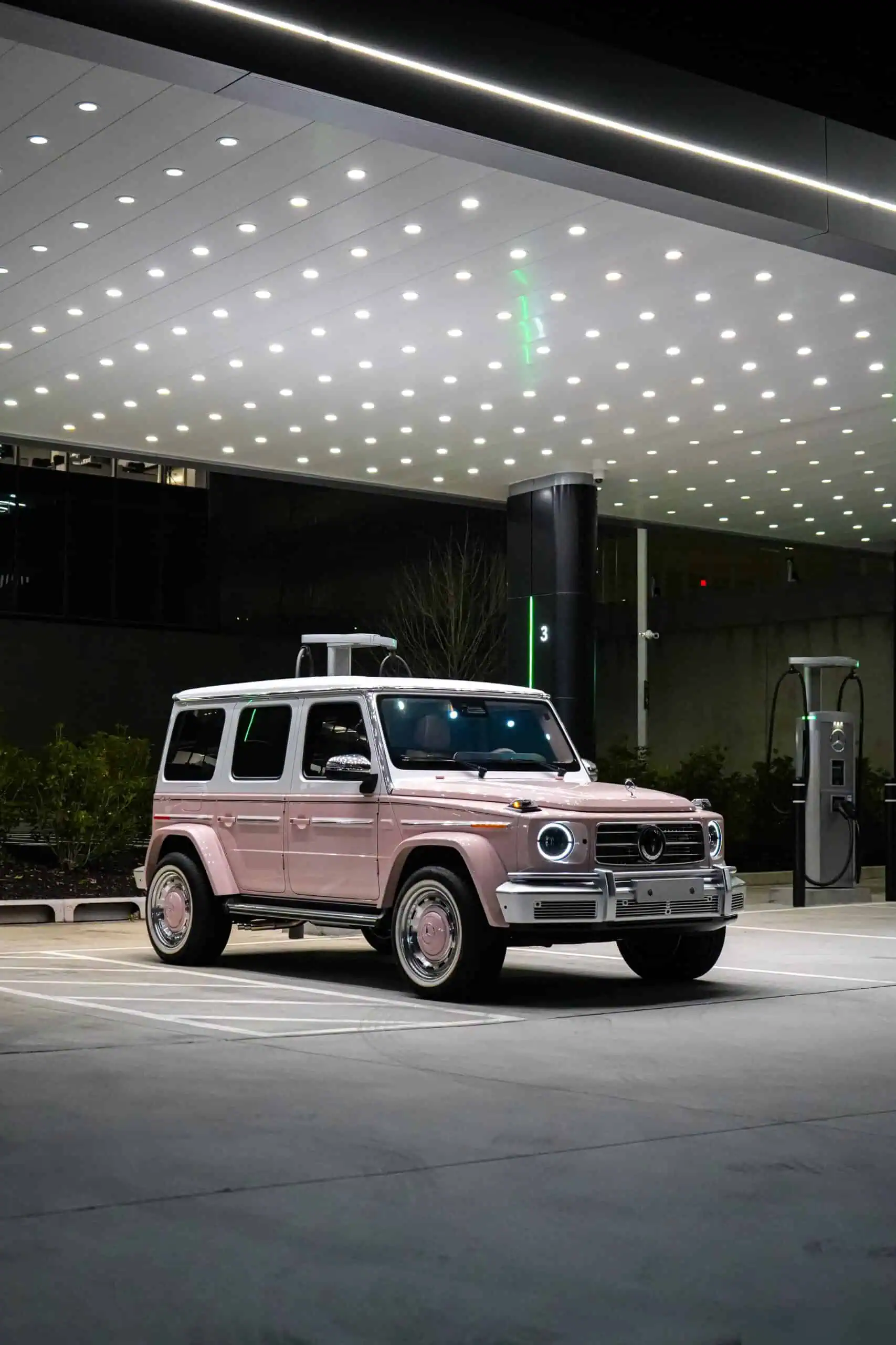 A sleek, pink electric vehicle parked under a modern, illuminated parking lot ceiling with LED lights, blending vintage design with contemporary electric mobility tech.