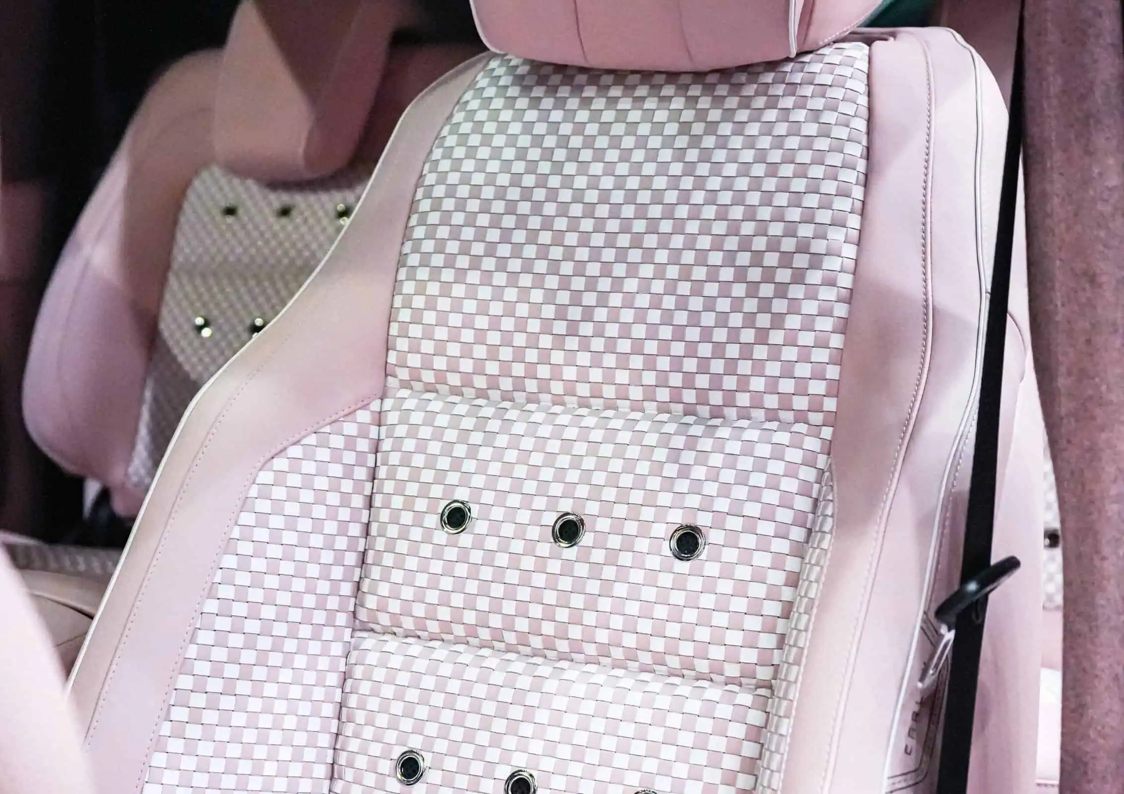 Close-up of a pink vintage modern car seat with checkered upholstery and decorative button details, showcasing stylish and comfortable design for luxury vehicle interiors.