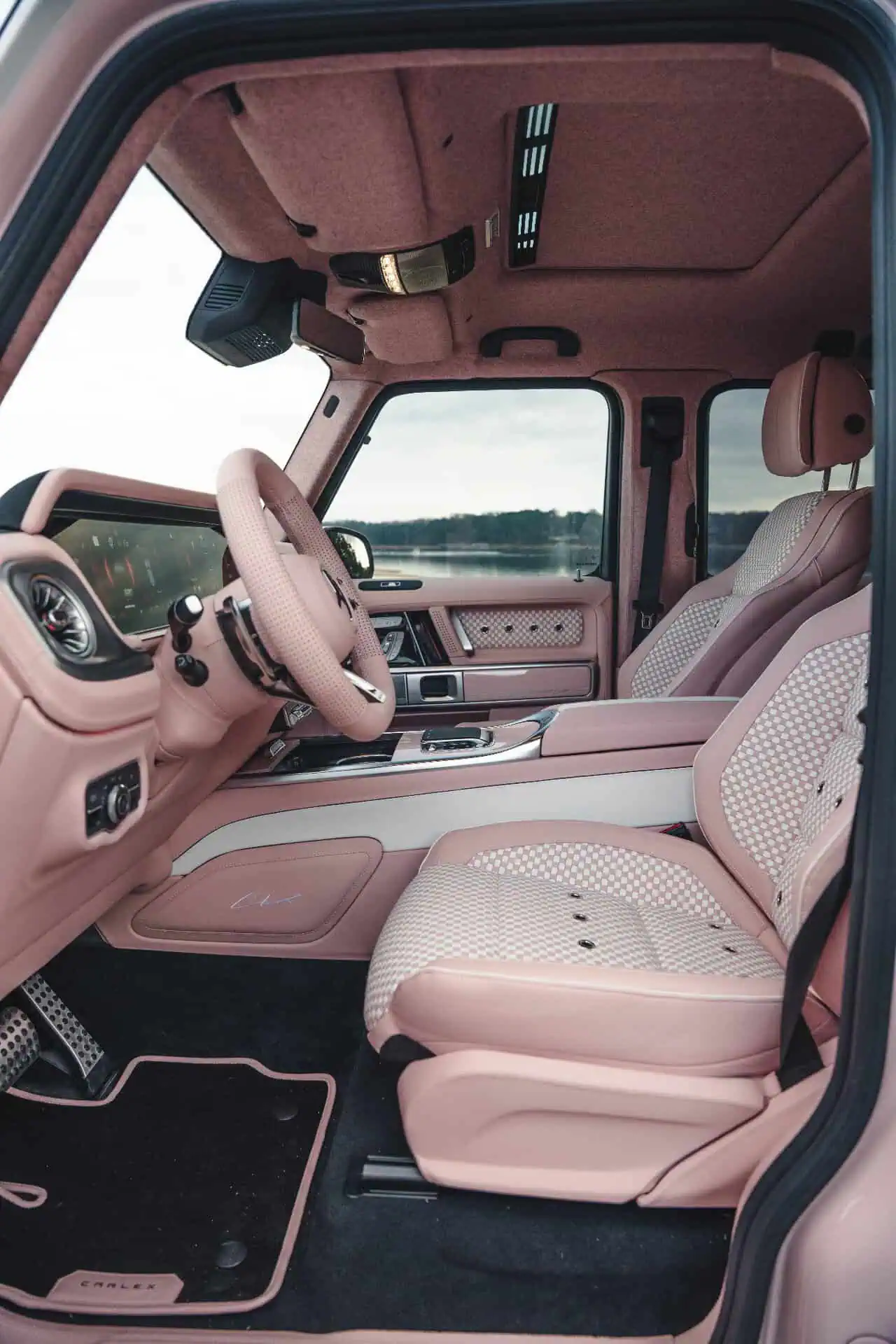 Luxurious vintage-modern vehicle interior with pink upholstery, detailed dashboard, and scenic lakeside view outside.
